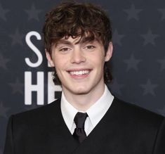 a young man wearing a black suit and tie smiling at the camera with stars in the background