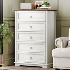 a white chest of drawers sitting next to a chair and potted plant in a living room