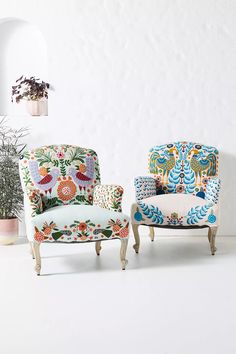 two colorful chairs sitting next to each other in front of a wall with potted plants