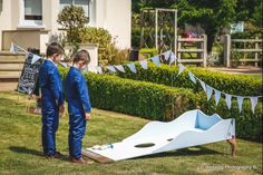 two boys in blue suits standing next to an upside down toy boat on the grass