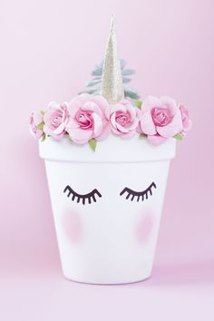 a white flower pot with pink roses and a unicorn's face painted on it