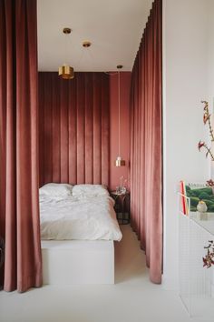 a white bed sitting under red curtains next to a tall window with pink drapes