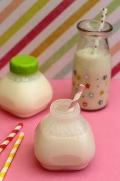 two milk bottles with straws next to them on a pink surface