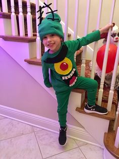 a little boy in a green costume standing on the stairs