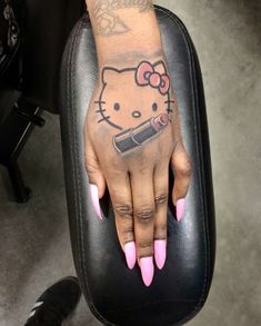 a hello kitty tattoo on the hand of a woman with pink nails and nail polish