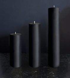 three black cylindrical candles sitting on top of a table