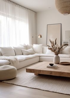 a living room with white couches and pillows on top of the rugs, in front of a large window