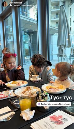 three children sitting at a table with plates of food and drinks in front of them