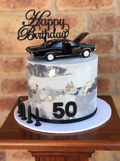 a birthday cake with a car on top and the number fifty written in gold foil