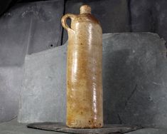 a brown jug sitting on top of a stone slab next to a gray rock wall