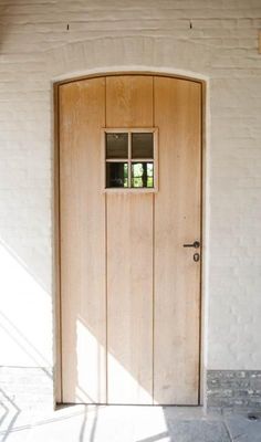 an open wooden door on the side of a white brick building with a small window