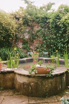 there is a small pond in the middle of this garden with flowers and plants around it