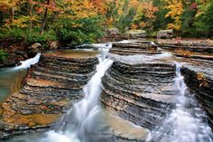 there is a waterfall in the middle of some rocks and trees with fall foliage around it