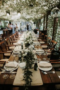 a long table is set with white flowers and place settings for an elegant dinner party