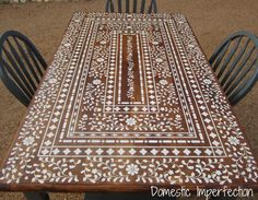 a wooden table with white and brown designs on it's top, sitting in front of two black chairs