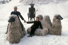 two men sitting on sheep statues in the snow with one man holding his hand out