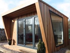 a small wooden building with glass doors on the front and side, in a garden area