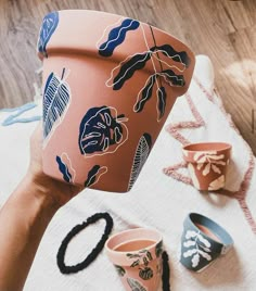 a hand holding a pot with plants on it next to other pots and cups sitting on the floor