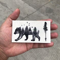 a person holding up a sticker with a bear and trees on the back of it