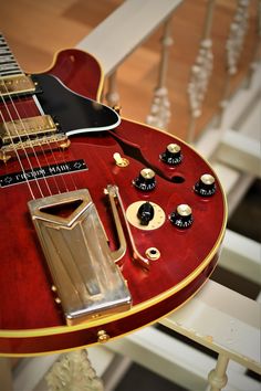 a red electric guitar sitting on top of a wooden table next to a stair case