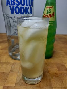 a glass filled with ice sitting on top of a wooden table next to two bottles