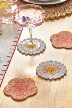 four coasters with flowers on them sitting on a table next to plates and glasses