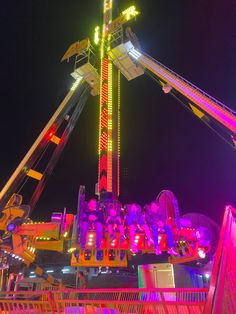 an amusement park ride at night with colorful lights on it's sides and people riding the rides