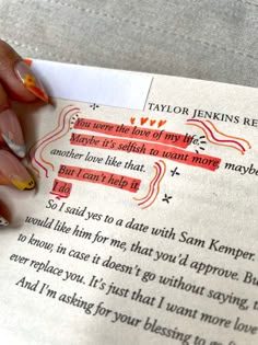 a woman's hand holding a piece of paper next to an open book with writing on it