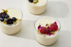 three desserts with fruit and flowers in them on a white counter top, one is garnished with raspberries