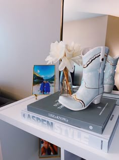 a pair of white boots sitting on top of a book next to a vase with flowers