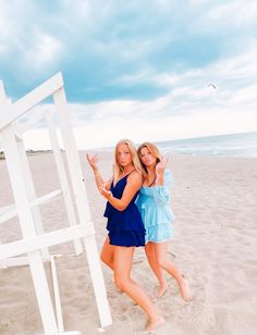 two beautiful young women standing on top of a sandy beach next to a white structure