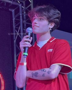 a man holding a microphone in his right hand and wearing a red shirt on stage