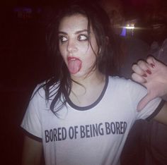 a woman sticking her tongue out while wearing a t - shirt that says bored of being bored