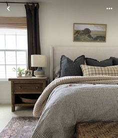 a bedroom with a bed, nightstand and window in the corner that has a painting on the wall above it