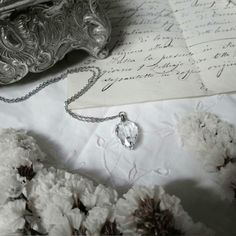 a close up of a necklace on a table with flowers and an old letter in the background