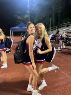 two young women in cheerleader outfits posing for the camera on a tennis court at night