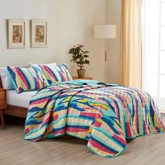 a bed with a colorful quilt on top of it next to a wooden dresser and window