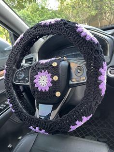 a car steering wheel cover with flowers on the front and center, in black and purple