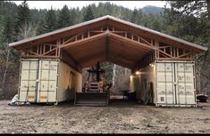 two large cargo containers sitting in the middle of a dirt field under a wooden roof