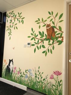 a cat sitting on a tree branch with flowers painted on the wall next to it