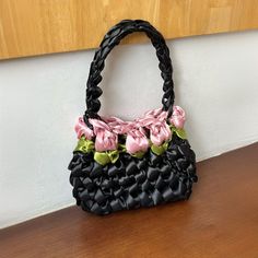 a black purse with pink flowers on it sitting on top of a wooden table next to a wall