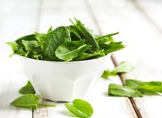 a white bowl filled with green leaves on top of a wooden table