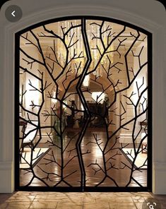 an open glass door with tree branches in the center and chandelier above it