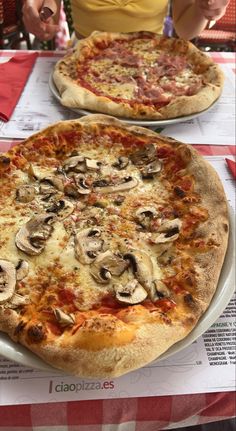 two pizzas sitting on top of a table covered in cheese and mushrooms next to each other