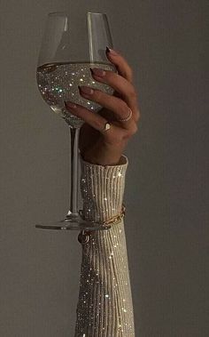 a woman's hand holding a wine glass in front of her face with glitter on it