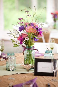 a vase filled with purple and pink flowers sitting on top of a table next to wine glasses