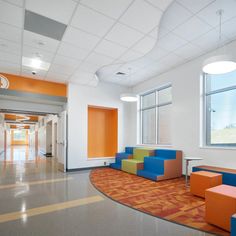 an empty hallway with brightly colored furniture and large windows