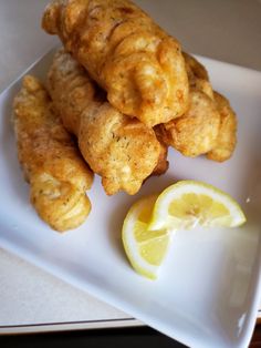 some fried food on a white plate with lemon wedges