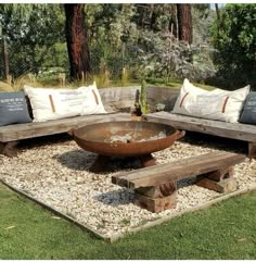 an outdoor seating area made out of wood and gravel with pillows on the back, surrounded by trees