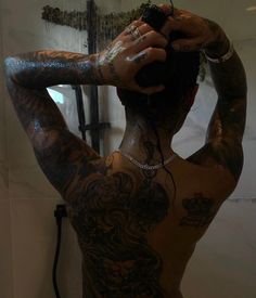 a man with tattoos on his back standing in front of a shower head and arm